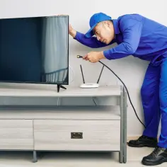Technik w niebieskim uniformie pokazuje, jak podłączyć światłowód do telewizora, podłączając kabel do routera.