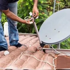 Instalator na dachu podłącza antenę satelitarną. Potrzebne będą: jedna antena, dwa telewizory i dwa zasilacze do odbioru sygnału.