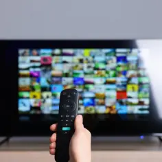 Dłoń trzymająca pilot przed ekranem telewizora z mozaiką obrazów. Zastanawiasz się, jaka częstotliwość TV naziemnej zapewni najlepszy odbiór?