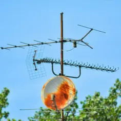 Rdzawe, zardzewiałe anteny telewizyjne i mała antena satelitarna na tle błękitnego nieba.