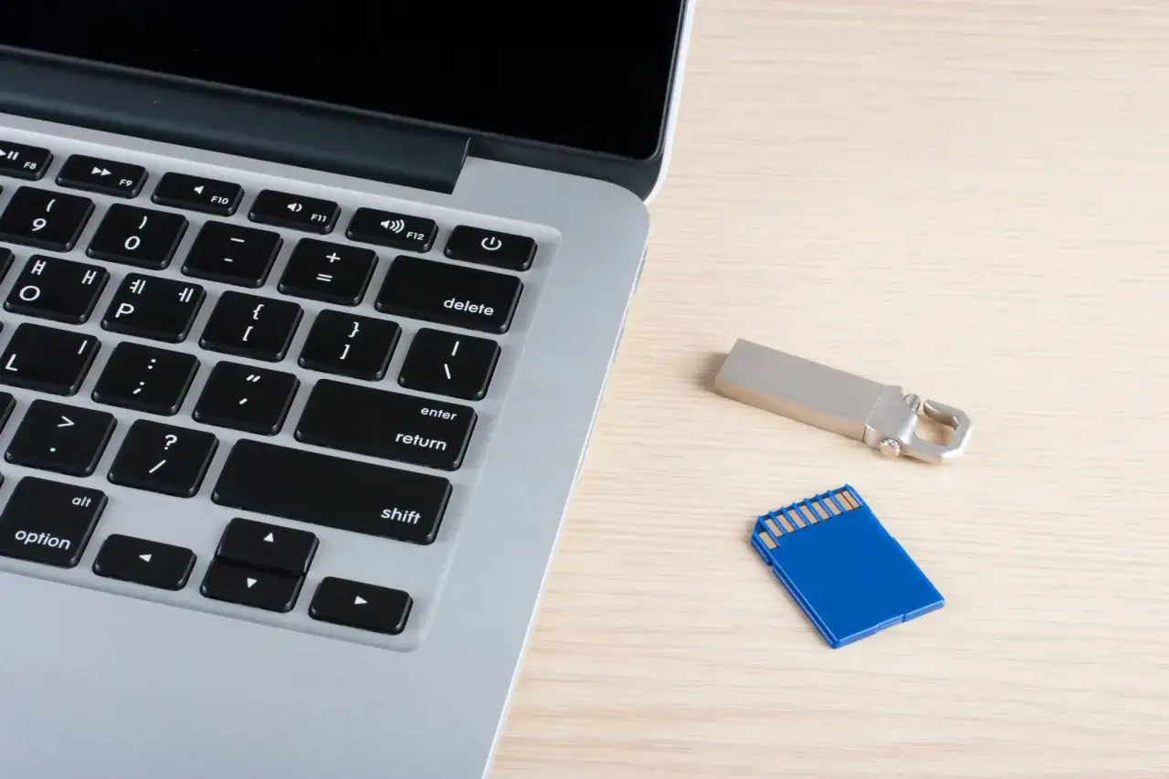 Klawiatura MacBook, pendrive i karta SD na drewnianym blacie. Gdzie znaleźć pendrive na Macu? Tutaj!