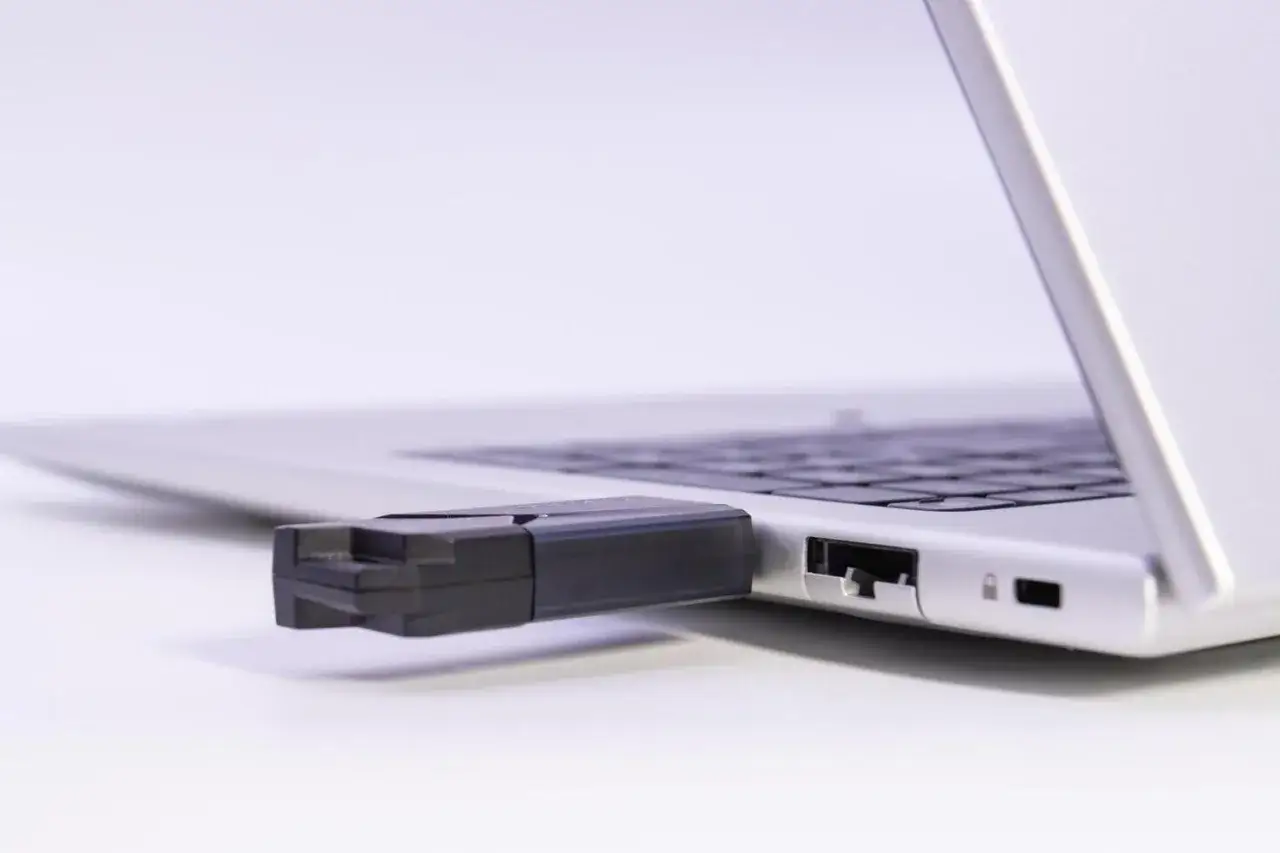 Czarny pendrive podłączony do portu USB laptopa. Prosty sposób, jak podłączyć pendrive do komputera, by przenieść dane.
