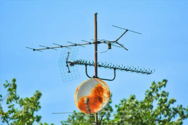 Rdzawe, zardzewiałe anteny telewizyjne i mała antena satelitarna na tle błękitnego nieba.